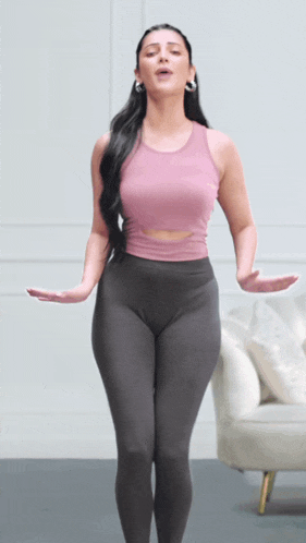 a woman in a pink tank top and grey leggings is dancing