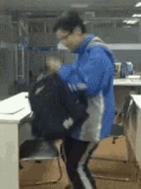 a man in a blue jacket is standing in front of a desk holding a backpack .