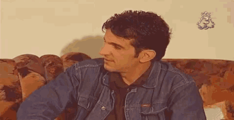 a man in a denim jacket is sitting on a couch with his arm outstretched .