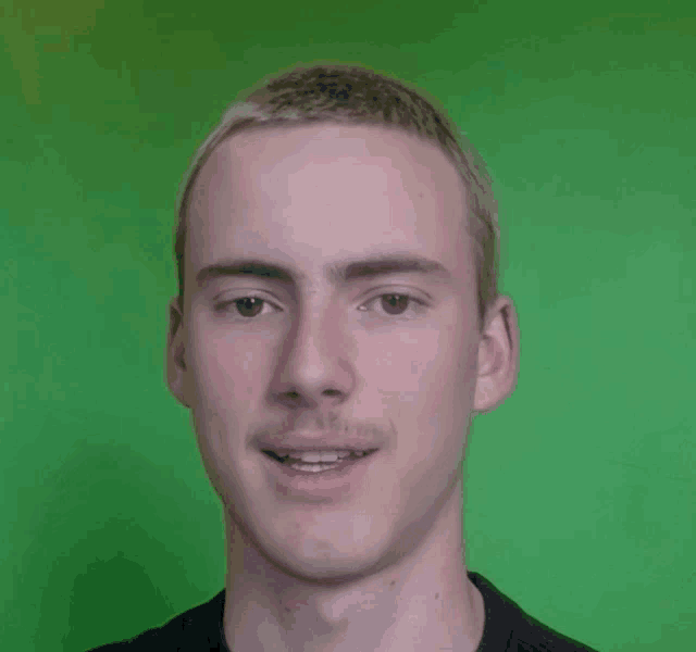 a man with short hair and a mustache is smiling in front of a green background