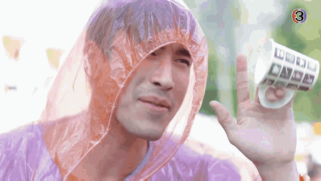 a man wearing a plastic raincoat holds a cup with the number 3 on it