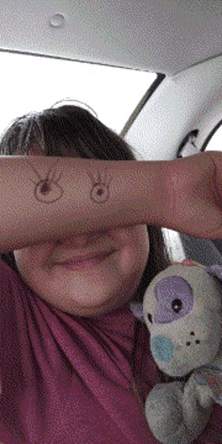 a girl is holding a stuffed animal and covering her face with her hand