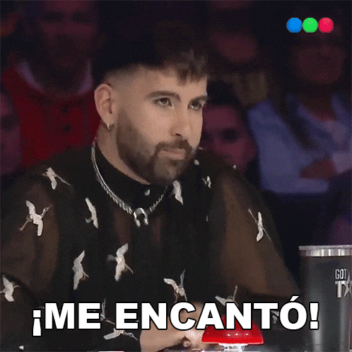 a man with a beard is sitting in front of a red button that says me encanto