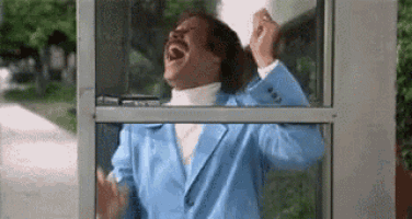 a man in a blue suit is laughing while standing in a pay phone booth .