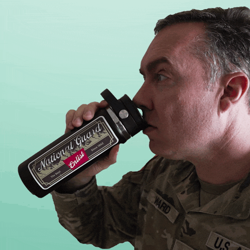 a man in a military uniform is drinking from a bottle that says national guard on it
