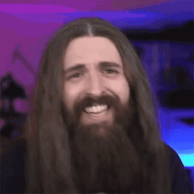 a man with long hair and a beard is smiling and looking at the camera .