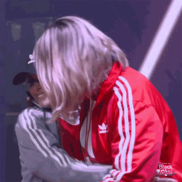 a woman wearing an adidas jacket is hugging another woman