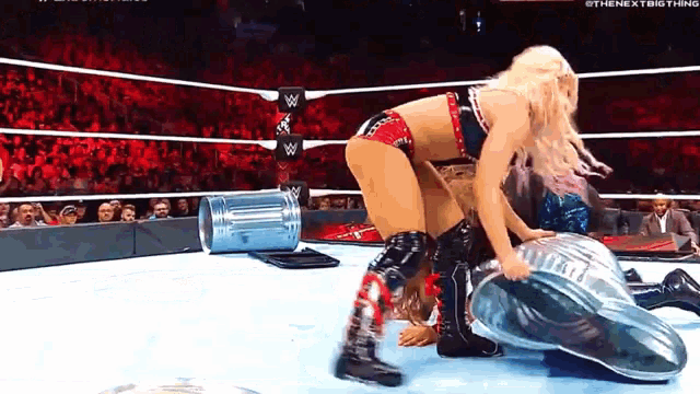 a woman is wrestling another woman in a wrestling ring with a trash can in the background .