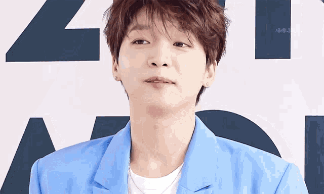 a young man wearing a blue jacket and a white shirt looks at the camera