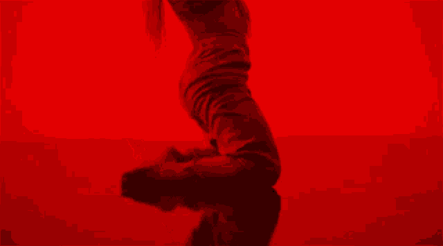 a woman in a red dress is doing a handstand in front of a red background .