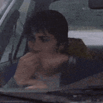 a man smoking a cigarette while sitting in the driver 's seat of a car