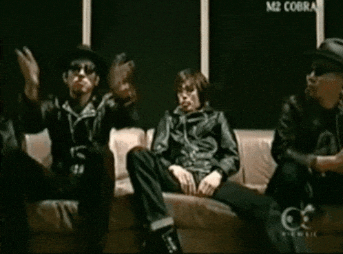 a group of people sitting on a couch with a m2 cobra sign in the background
