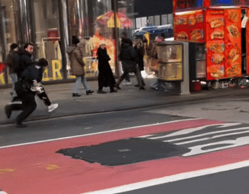 a group of people are walking down a street in front of a store with the letter r on the front
