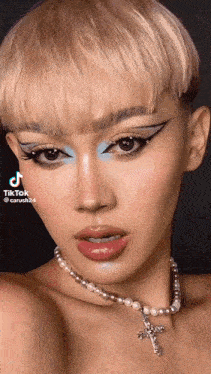 a woman wearing a pearl necklace with a cross on it is looking at the camera .