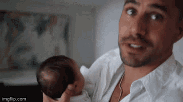 a man in a white shirt is holding a baby in his arms and smiling .