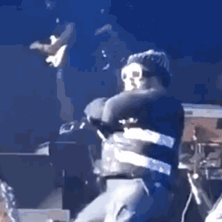 a man is hugging another man on a stage while another man plays a guitar .