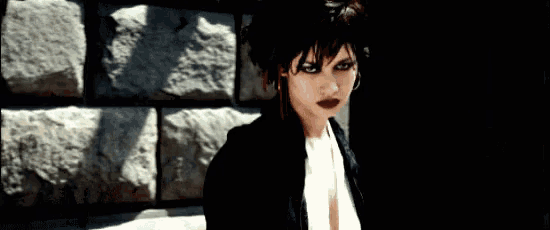 a woman in a black jacket and white shirt stands in front of a stone wall