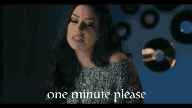 a woman stands in front of a wall with records and the words one minute please