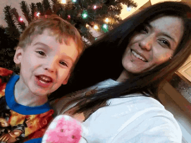 a woman and a boy are smiling in front of a christmas tree
