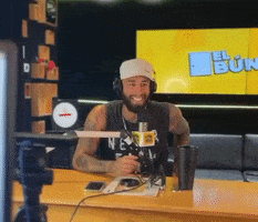 a man is sitting at a desk with a microphone in front of a screen that says el bun on it