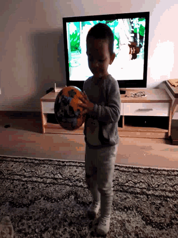 a little boy holds a ball in front of a television