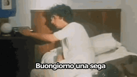 a man is sitting on a bed with the words buongiorno una sega written above him .