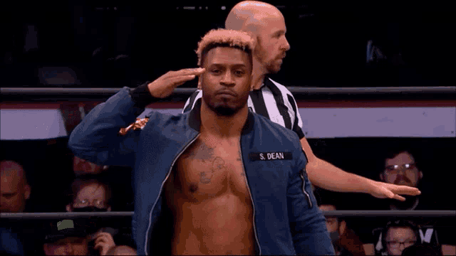 a man in a blue jacket with the name s. dean on his chest is standing in a wrestling ring .