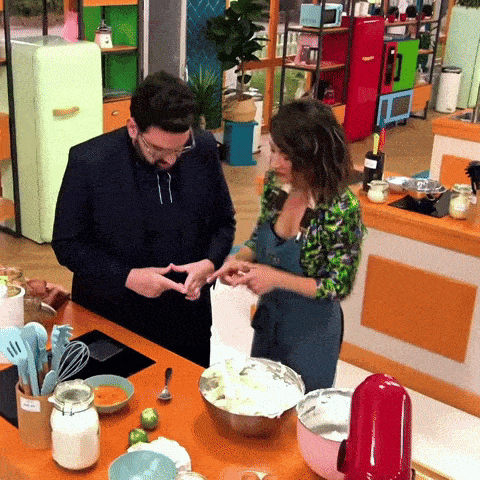 a man and a woman are cooking in a kitchen and the woman is wearing a green shirt