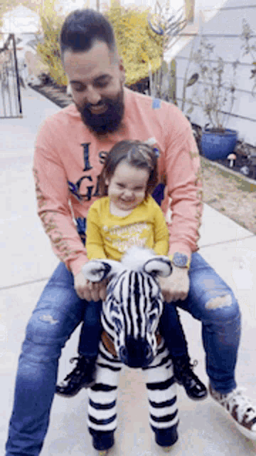 a man with a beard is holding a little girl on a zebra ride