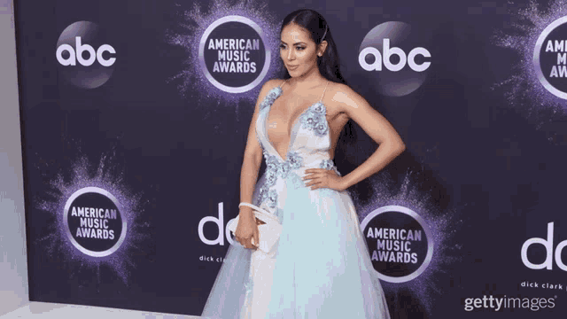 a woman in a blue and white dress stands on a purple carpet for the american music awards
