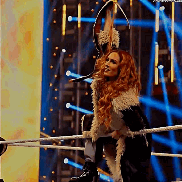 a woman in a fur coat is standing in a wrestling ring holding a sword .