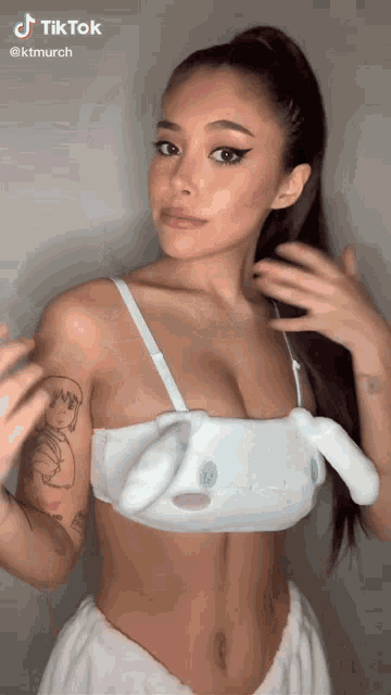 a woman with a tattoo on her arm is wearing a white bra with bunny ears on it .