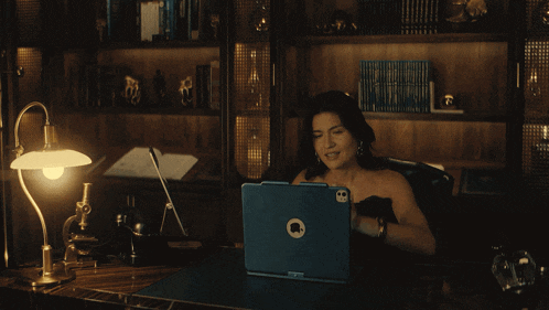 a woman sits at a desk with an apple laptop on her lap