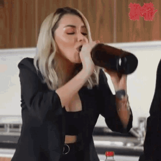 a woman in a black jacket is drinking from a bottle .