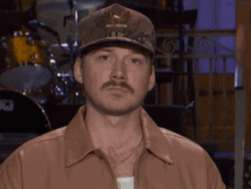 a man with a hat and a mustache is wearing a brown shirt