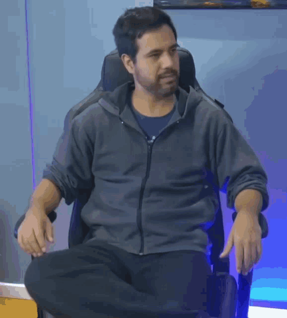 a man in a grey jacket is sitting in an office chair with his legs crossed