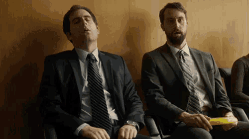 two men in suits and ties are sitting next to each other in a waiting room .