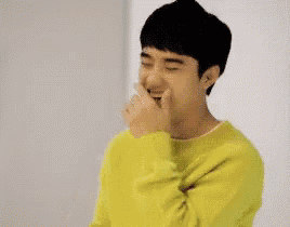 a young man is wearing a yellow sweater and covering his mouth with his hands .