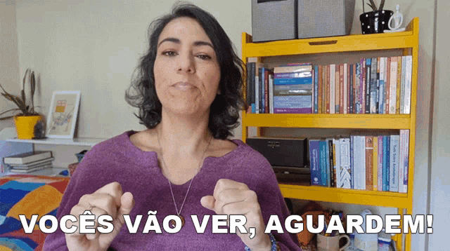 a woman stands in front of a yellow bookshelf and says " vocês vão ver aguardem "
