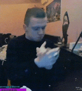 a man in a black shirt is sitting at a table with his hands folded