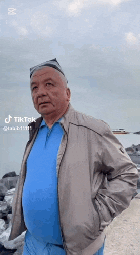 an older man wearing a blue shirt and a jacket is standing on a beach .