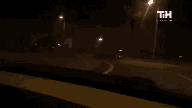 a car is driving down a street at night with a t.i.h. logo behind it