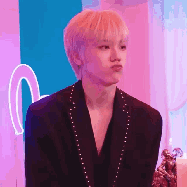 a young man with pink hair is making a funny face while wearing a black jacket .