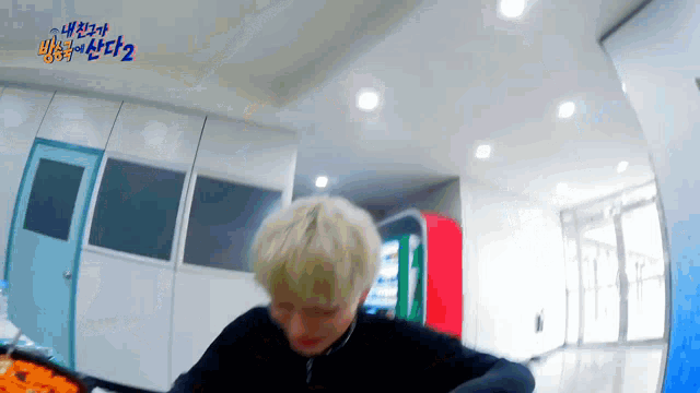 a man with blonde hair is standing in a hallway with a red vending machine