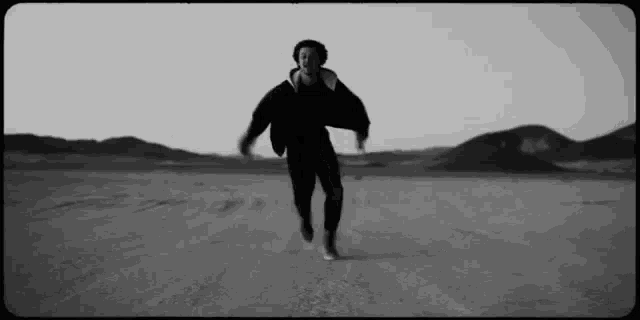 a black and white photo of a man running on a dirt road in the desert .