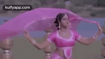 a woman in a pink saree is dancing in front of a lake .