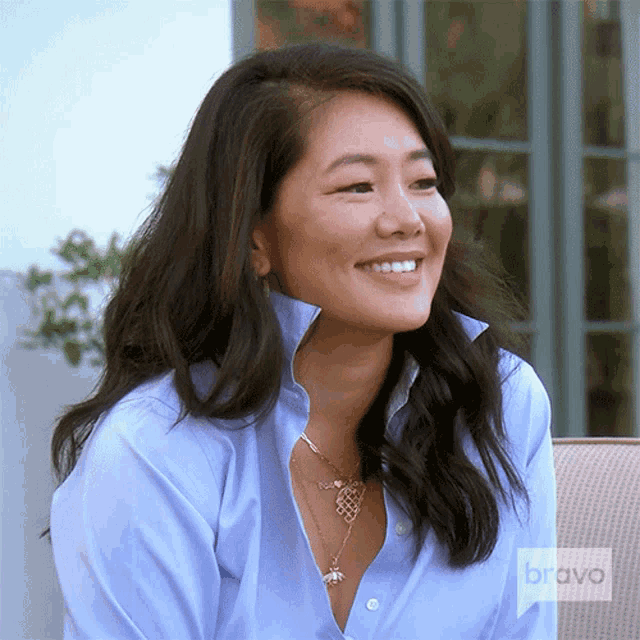 a woman wearing a blue shirt and a necklace is smiling while sitting on a chair .