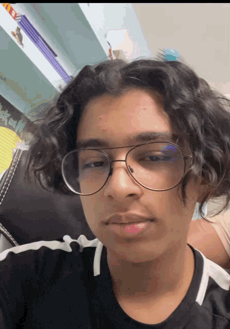 a young man wearing glasses and a black shirt with a white stripe on the sleeve