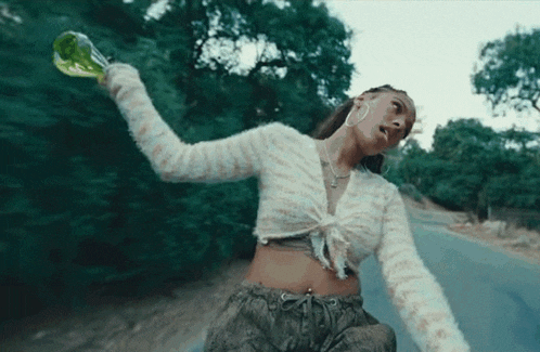 a woman is riding a skateboard down a road while holding a green bottle in her hand .