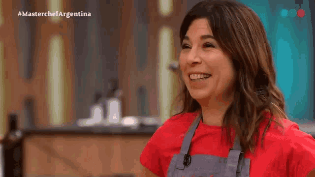 a woman wearing a red shirt and an apron is laughing and pointing at something .